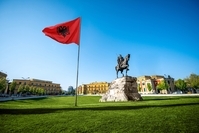 Tirana Die albanische Flagge in Tirana neben einer Statur mit blauem Himmel im Hintergrund